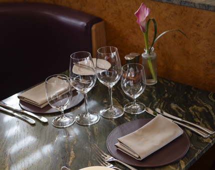 A close up of a set table in The Lighthouse Restaurant. there is a vase with a single pink flower in it. 