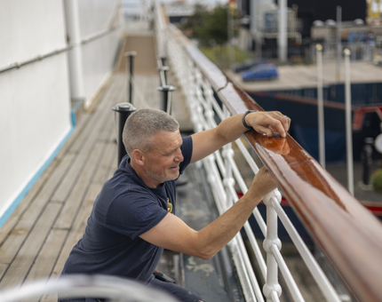 On the deck of Britannia, a maintenance team member is attaching a handrail. 