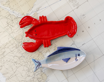Two trinket trays, one is shaped like a red lobster, the other is a blue fish. 