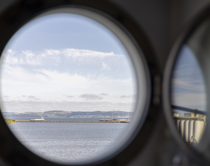 Through the round porthole, a view over the water to hills beyond. 