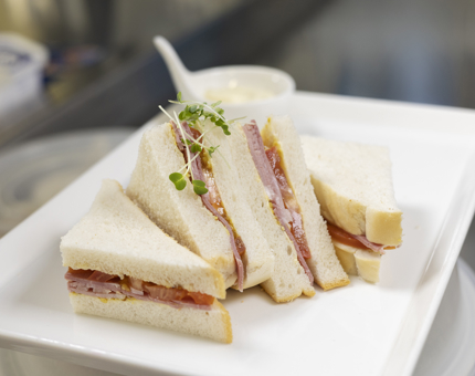 A Ham and tomato sandwich on a white plate in the onboard Galley.
