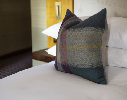 A tartan pillow sits on a bed with white covers aboard Fingal Hotel. 