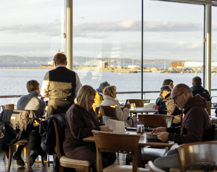 In the Royal Deck Tearoom visitors are sitting at tables next to large windows overlooking the Port of Leith. 