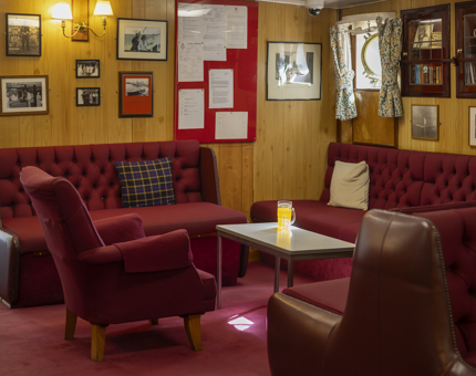A crew's mess with dark red carpet and seating. 