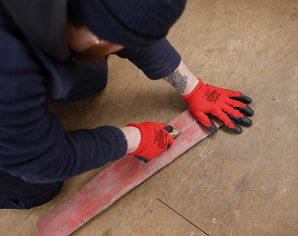 A maintenance man is cutting a piece of red fabric. 
