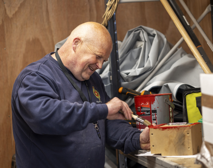 A Facilities Officer painting a wooden box with red paint. 
