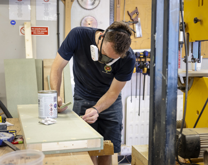 A maintenance man is adding wood filler to a shelf for the Tearoom office.