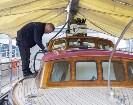 A maintenance man is on the Royal Barge, using a power sander to remove the varnish. 