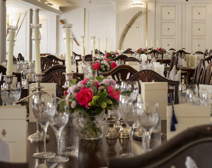 The State Dining Room aboard Britannia has it's tables set for an evening event. There are pink flowers on the tables. 