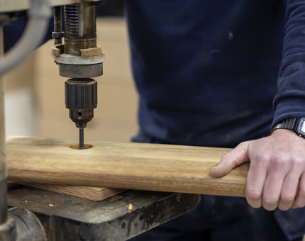 A close up of a Maintenance team member drilling a hole in a handrail. 