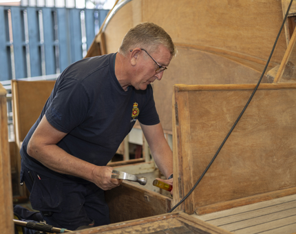 A maintenance man removing a piece of damaged wood from the Royal Barge.
