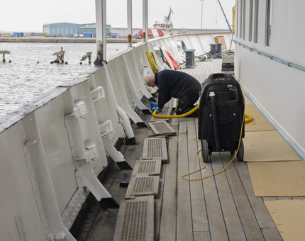A Maintenance team member kneeling on the deck cleaning the scuttlers.