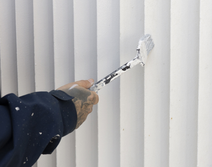 A close up of a hand holding a paint brush applying a coat of white paint. 
