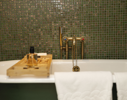A roll-top bath with a wooden tray is in a green tiled bathroom on Fingal Hotel in Leith. 