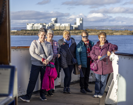 A groups of 5 ladies stand on Britannia's Bridge, the Port of Leith is behind them. 