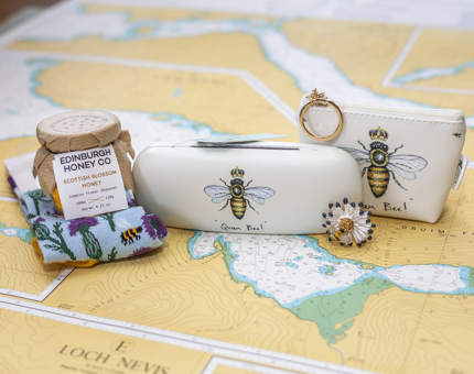 Bee themed items from the Shop. There is a glasses case, coin purse, Edinburgh Honey Co. Scottish blossom honey, and socks. 