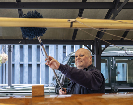 A Facilities Officer is dusting a small sail boat on Britannia's quayside. 