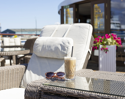 On Fingal's Deck in the Port of Leith, an iced latte is on a table next to a lounge chair in the sunshine. 