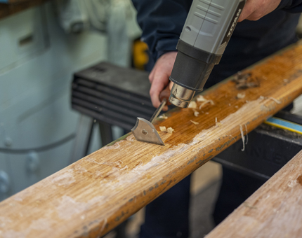 A member of the Maintenance team using a heat gun to remove varnish from a wooden handrail. 