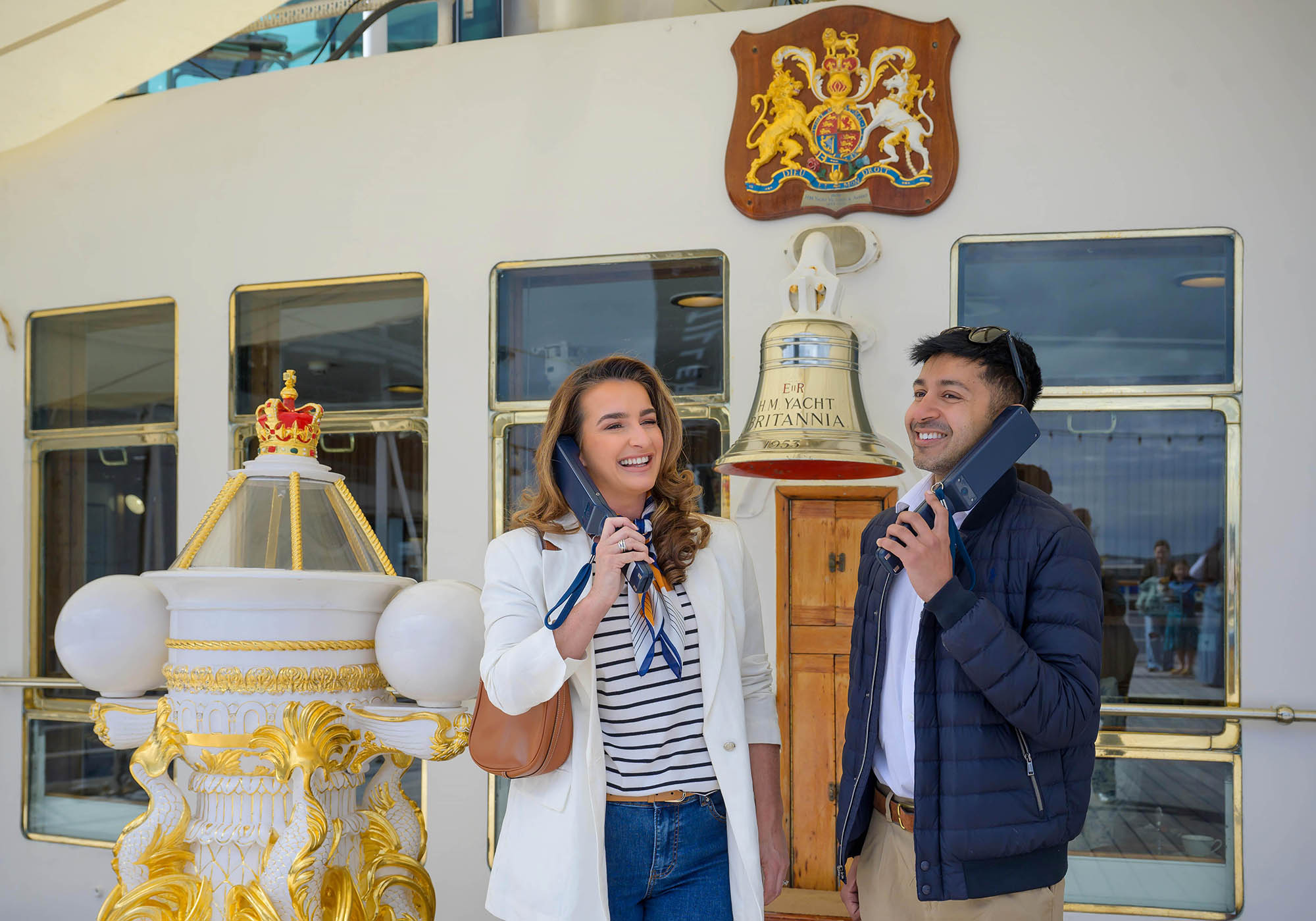 A woman and a man listen to handheld audio guides at The Royal Yacht Britannia. 
