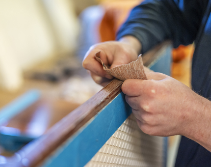 A close-up of hands sanding a step from the Royal Barge. 