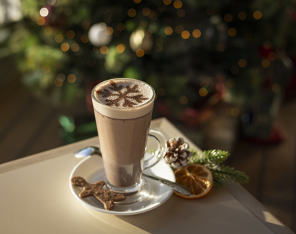 A hot chocolate in a tall glass with a gingerbread man biscuit on the plate. 