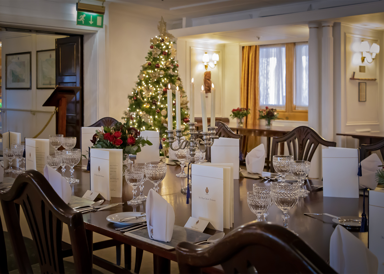 The State Dining Room with the tables set and a lit up Christmas tree in the corner. 